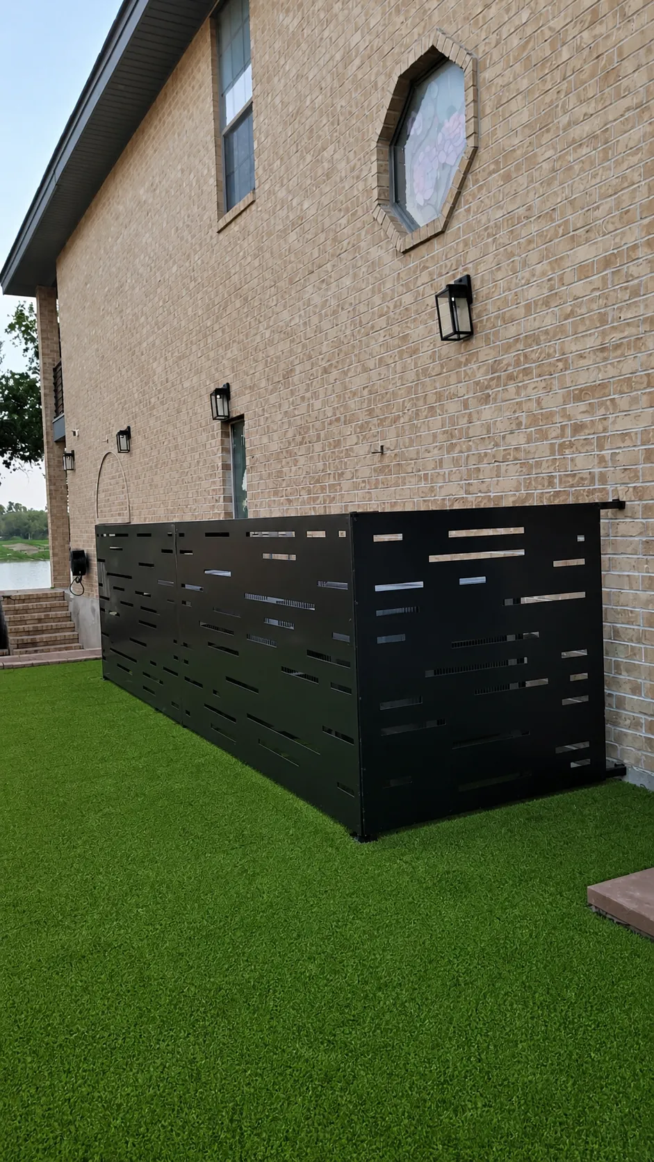 Black aluminum equipment screen installed beside a brick home